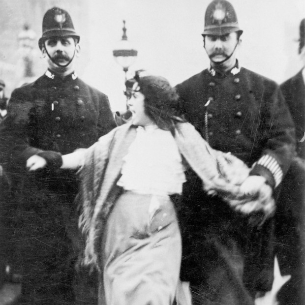 A 'Lancashire lassie' being escorted through the palace yard, Westminster Palace, London, 20th March 1907. A young woman is reluctantly escorted by two policeman who are holding her by the arms. The woman is still protesting as she is led away. The last line of the verse at the bottom says 'For Women's Rights anything we will dare; Palace Yard, take me there!' (Photo by Museum of London/Heritage Images/Getty Images)